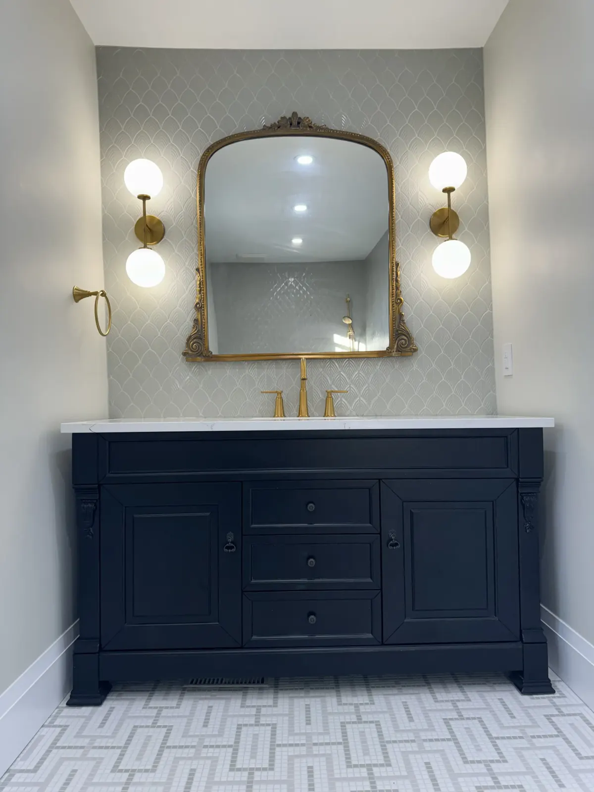 Navy vanity with antique gold mirror and marble herringbone floor