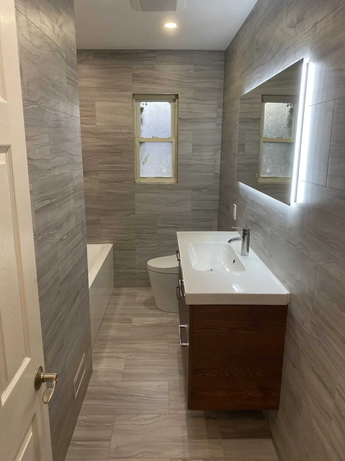 Long bathroom with stone-look tile and walnut vanity